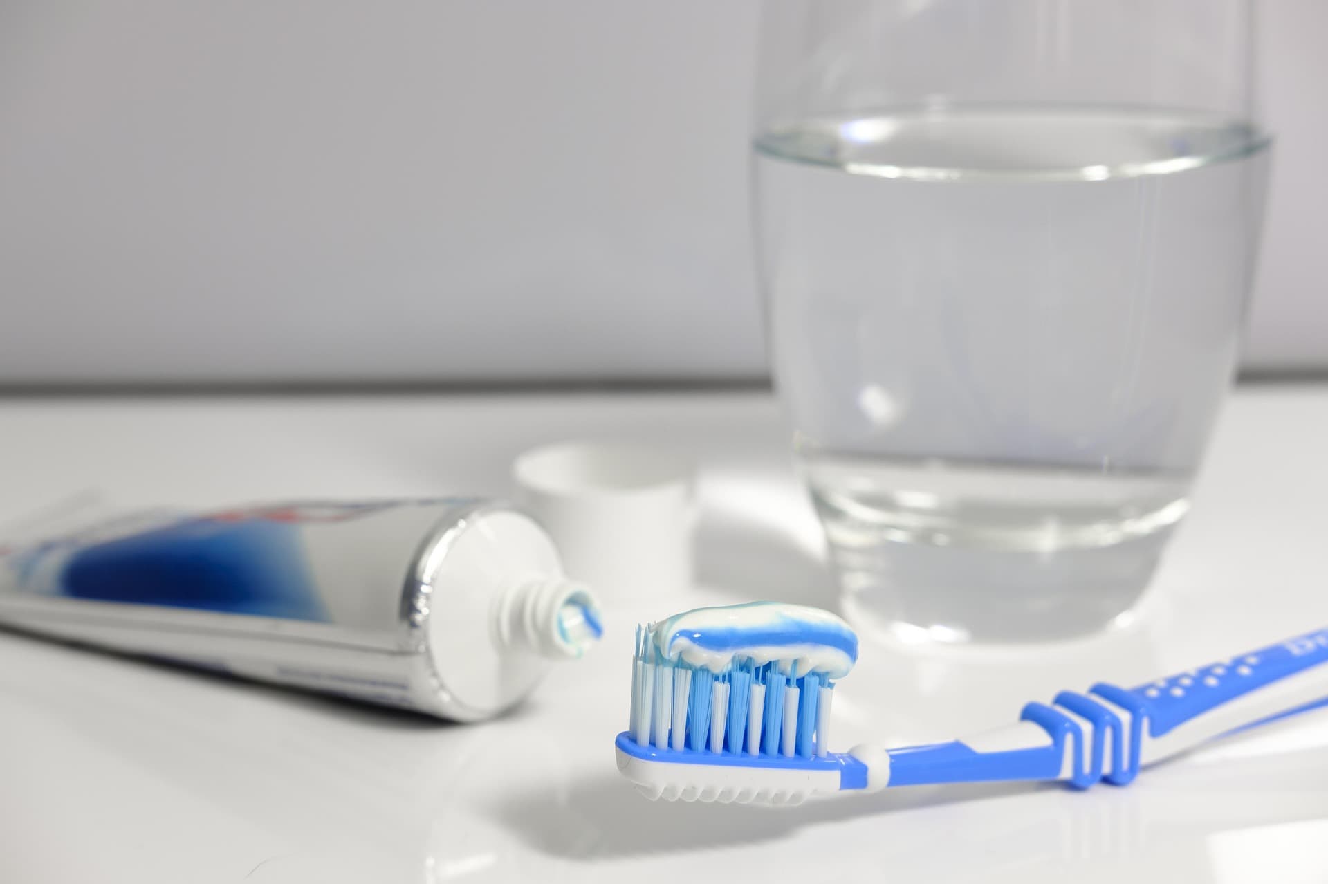 Un cepillo de dientes, una pasta de dientes y una vaso transparente con agua