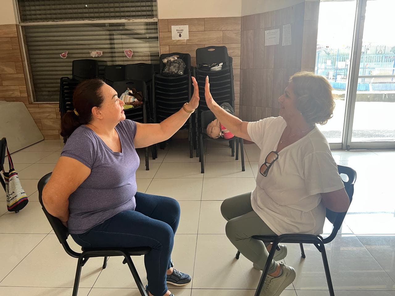 dos mujeres sentadas a punto de tocarse la mano, y con una mano atrás de la espalda