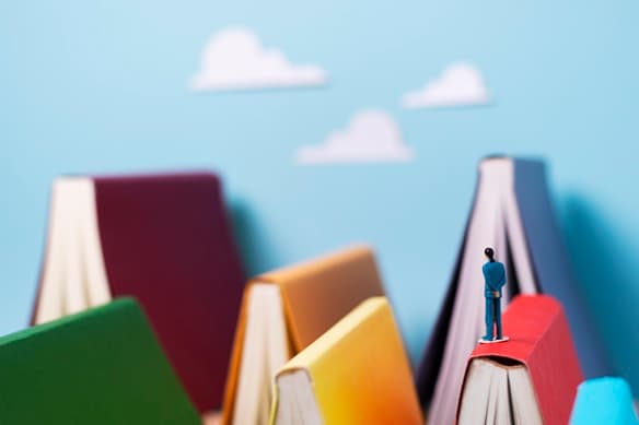 Varios libros colocados como en forma de techos y una figura humana sobre uno de los lomos